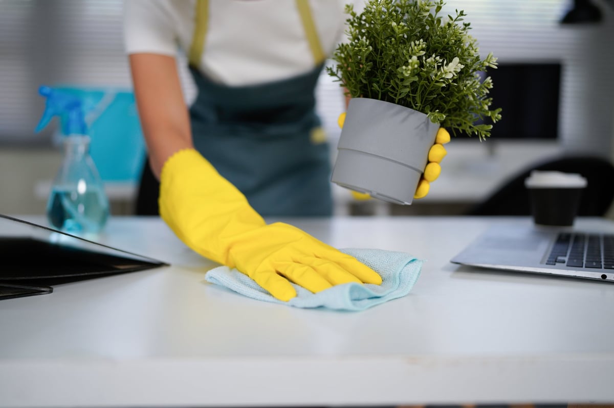 young woman in yellow gloves cleaning the table in the office.